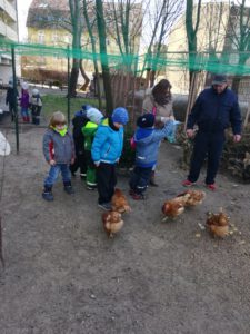 Einige Kinder in warmer Kleidung und zwei Erwachsene stehen bei den die Hühnern im Hof