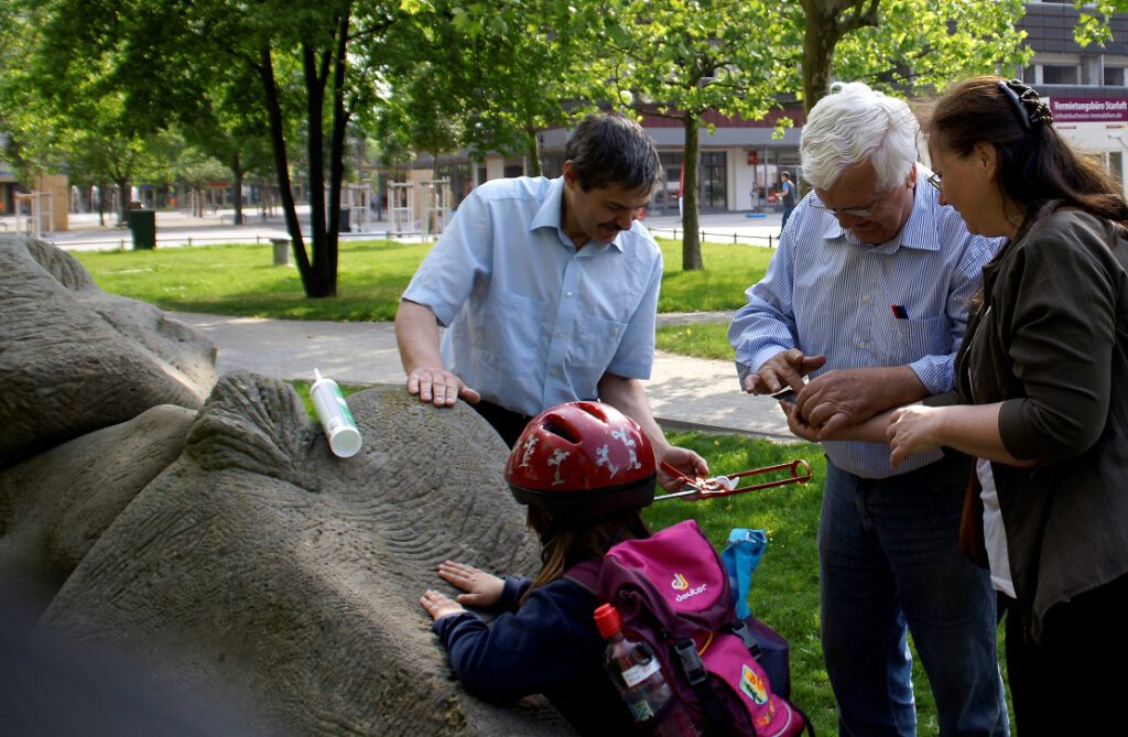 Menschen stehen im Freien vor einer Skulptur, ein Kind ist auch dabei