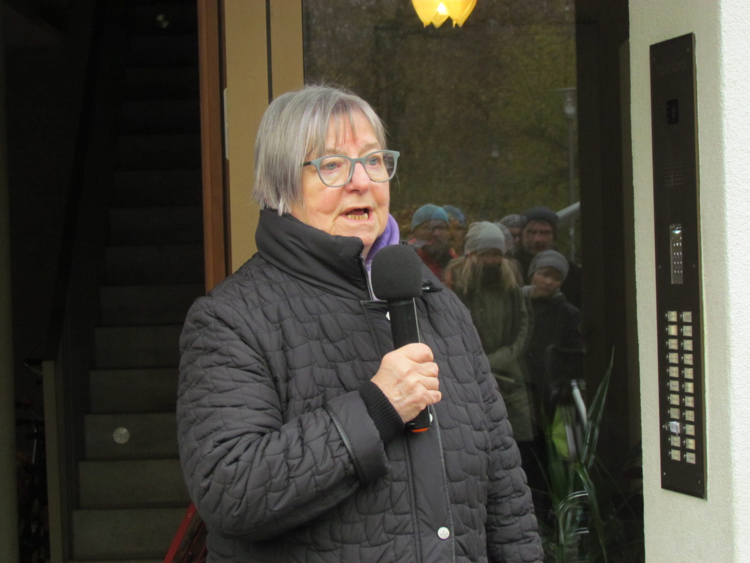Dagmar Poetzsch berichtet über das Schicksal von Auguste und Ignatz Schnee, sie steht mit einem Mikrofon vor einem Wohnhaus