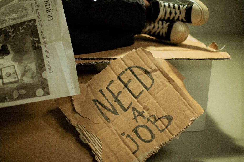 ein Pappschilf mit Füßen auf dem steht: need a job