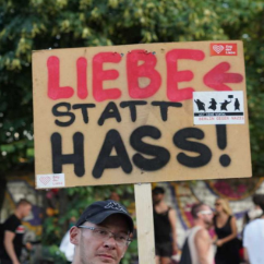 Auf dem Bild ist ein Mann zu sehen, der ein Plakat in die Luft hält. Dort steht drauf "Liebe statt Hass".