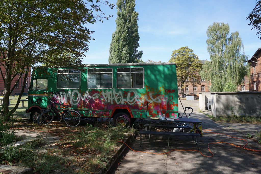 Ein alter, grüner Bus mit Graffiti bemalt, steht auf einer Rasenfläche unter einem Baum.