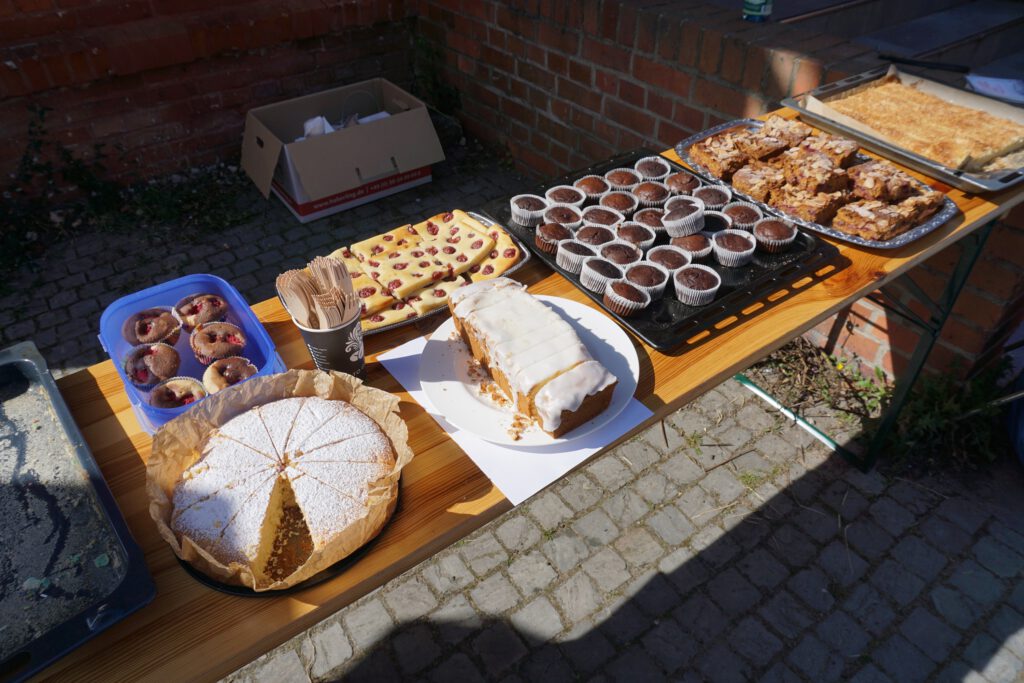 Auf einem Biertisch stehen verschiedene Kuchensorten und Muffins auf Tabletts und Kuchenblechen.
