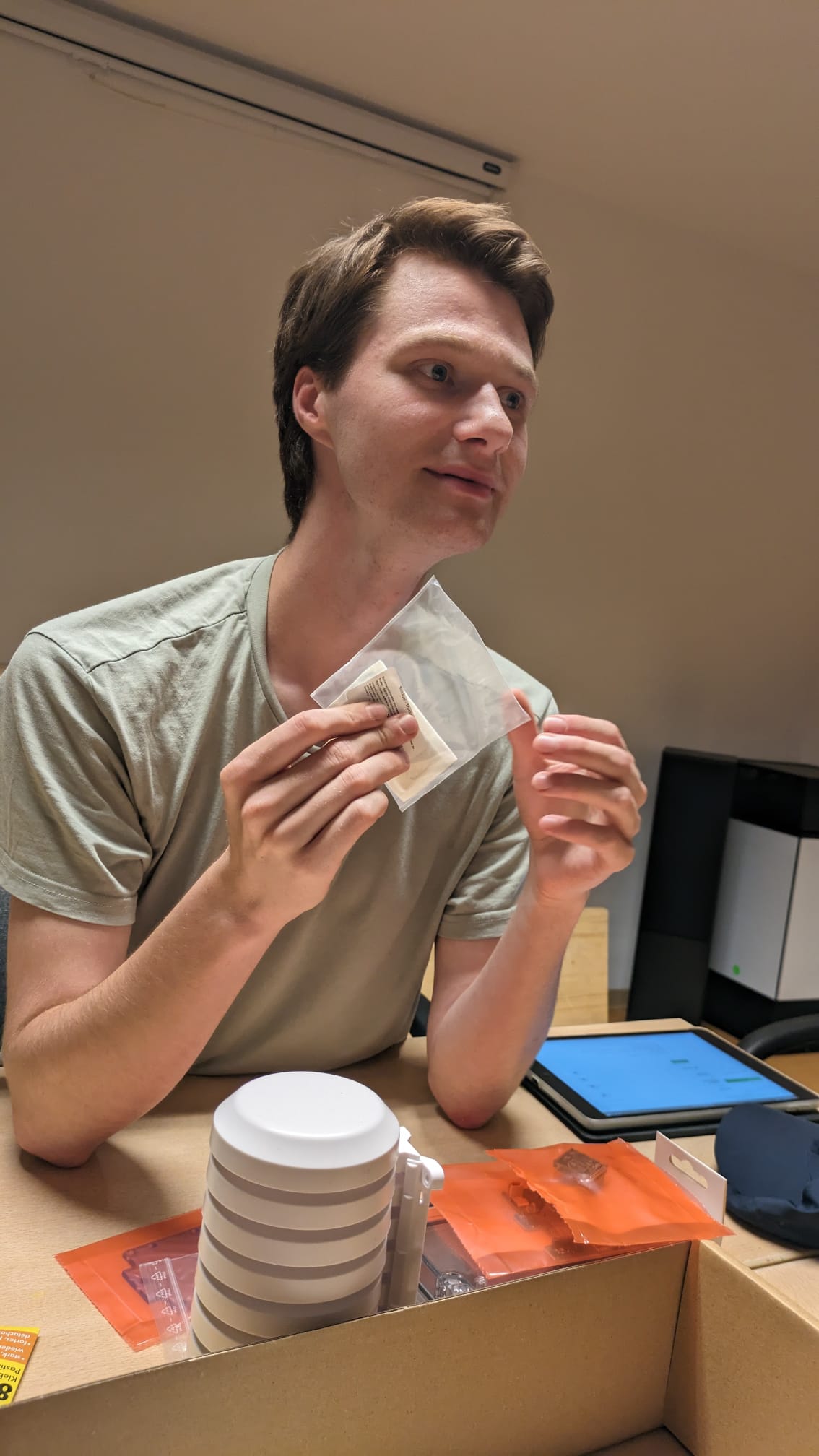 Ein junger Mann sitzt am Tisch, auf dem technische Kleinteile liegen.