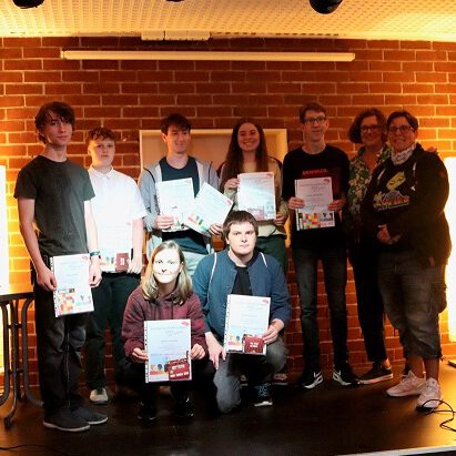 Mehrere Jugendliche, fünf Jungs und zwei Mädchen, haben sich zu einem Gruppenfoto aufgestellt. Ein Junge und ein Mädchen knien in der ersten Reihe. Alle haben eine Urkunde in den Händen und halten sie gut sichtbar vor der Brust. Sie haben sie gerade für den Jugendengagementpreis 2023 erhalten. Mit im Bild sind zwei erwachsene Frauen. Sie haben die Urkunden gerade übergeben.