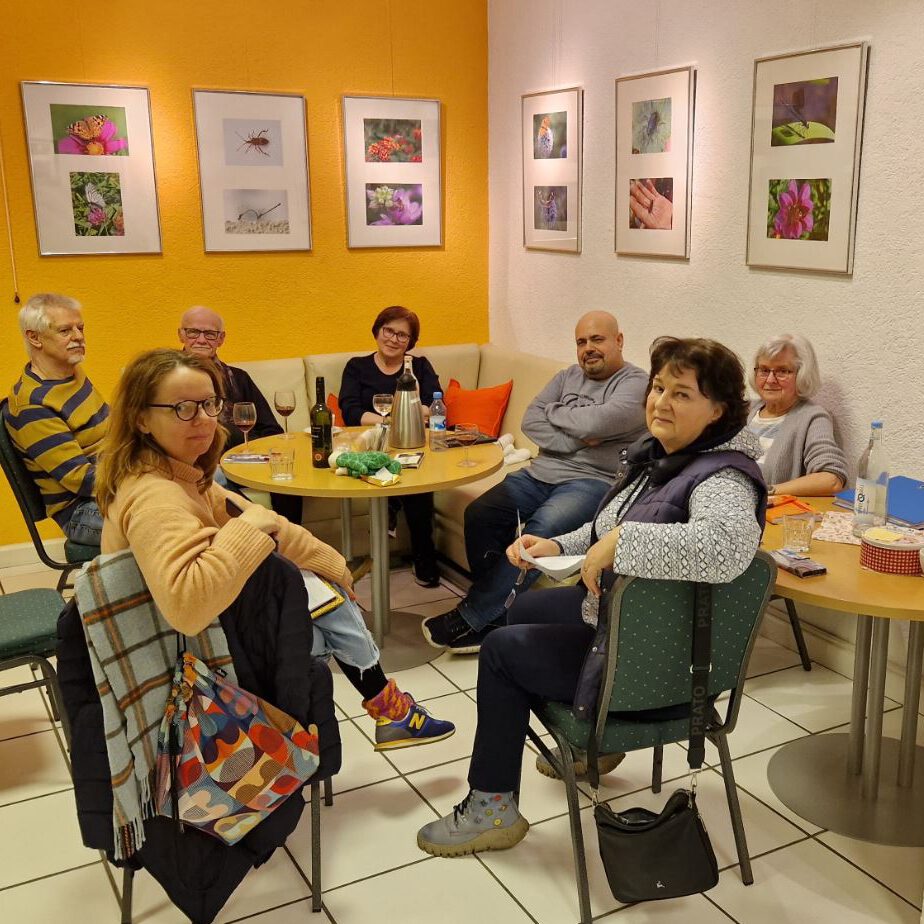 Mitglieder des Galerie-Teams sitzen für eine Besprechung um einen runden Tisch. Im Hintergrund hängen Kunstwerke an den Wänden.