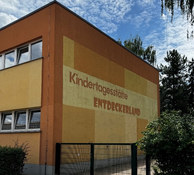 Außenansicht der Kindertagesstätte Entdeckerland. Ein zweigeschossiges Haus mit Bemalung in verschiedenen Orangetönen.