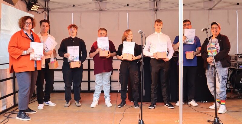 6 junge Preisträger stehen nebeneinander auf der Bühne und zeigen ihre Urkunden in die Kamera.