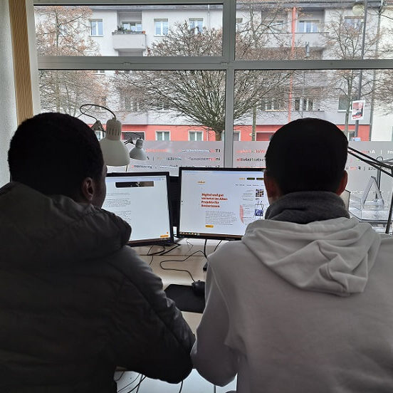 zwei Schüler sitzen mit dem Rücken zum Betrachter vor dem Computer.