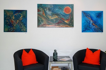Drei Acrylgemälde hängen nebeneinander an einer Wand. Alle haben einen blauen Grund und darauf abstrakte Formen und Linien in Beige, Braun und Orange.