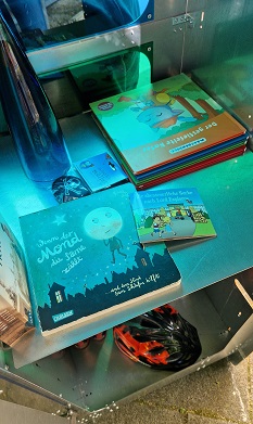 Kinderbücher liegen im Findus-Tauschschrank und werden von bläulichem Licht beschienen, das durch das gefärbte Plexiglas kommt.