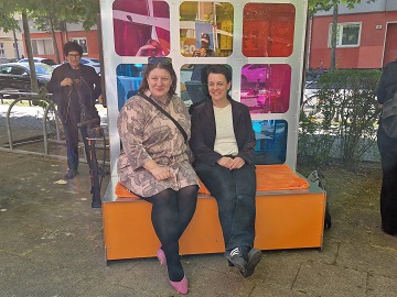 Petra Grampe von der Stiftung Stadtkultur und Jenny Stiebitz von der oskar freiwilligenagentur sitzen auf der Sitzbank vor dem Findus-Tauschschrank.