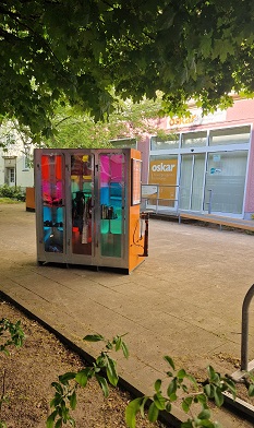 Der Rechteckige Findus-Tauschschrank mit bunten Fenstern steht auf dem Platz vor der oskar Freiwilligenagentur.