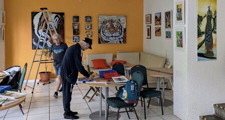 Zwei Mitglieder des oskar Galerie-Teams sind im Ausstellungsraum beschäftigt. An der Wand hängen bereits einige Bilder.