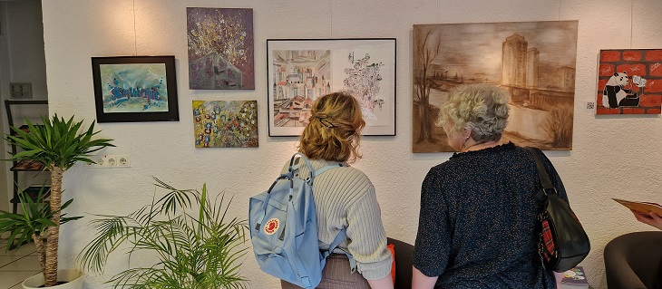 Zwei Besucherinnen der Ausstellung sehen sich Gemälde an der Wand an.