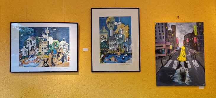 Drei Werke in der Ausstellung hängen an einer orangenen Wand. Zwei passen zusammen und zeigen typische Berliner Hinterhofszenen. Das rechte Gemälde zeigt eine graue Straßenszene im Regen mit Neon-Reklamen und einer Person, die im leuchtend gelben Regenmantel die Straße überquert.