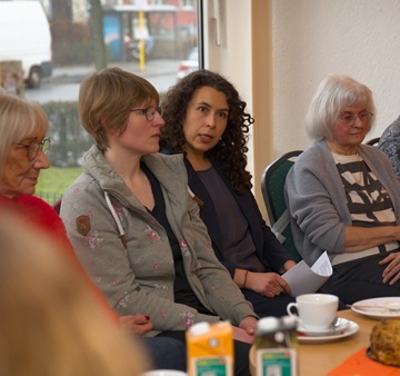 vier Frauen sitzen an einem Tisch nebeneinander und die eine Frau hält gerade eine Rede, was man an ihrem Gesicht erkennt.