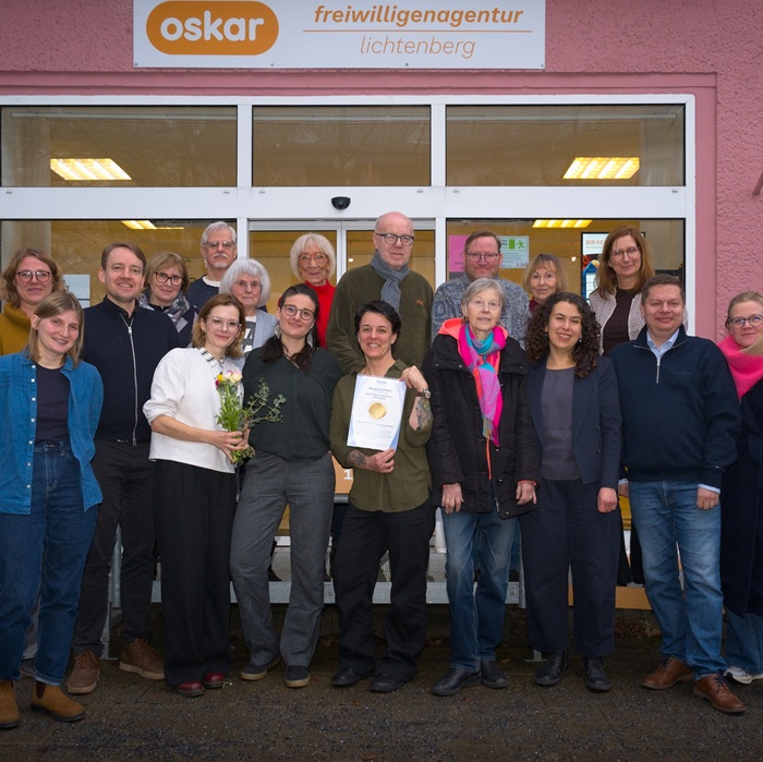 Eine Gruppe von Menschen steht in zwei Reihen vor einem Gebäude. Die Person vorne in der Mitte hält ein Blatt mit Logo des bagfa-Qualitätssiegels in Händen. Alle lächeln in die Kamera.