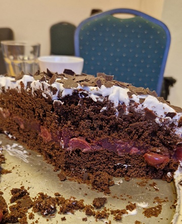 Bildausschnitt von einer halben Schwarzwälder-Kirschtorte. Sie ist schokoladig mit einem Streifen Kirschen in der Mitte und einer Sahneschicht mit Schokostreuseln oben drauf.