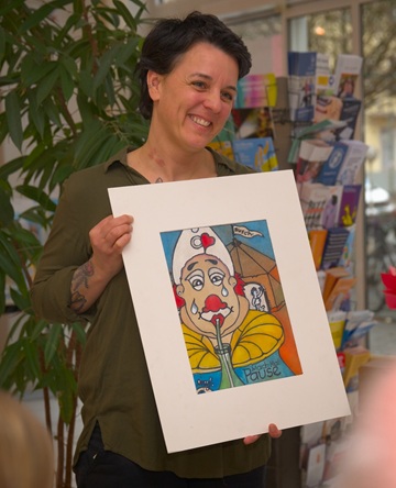 Eine Frau lächelt und hält ein Bild in der Hand. Es zeigt einen Clown mit Tränen vor einem Zirkuszelt.