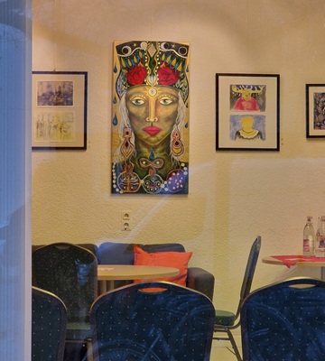 Blick durchs Fenster in den Ausstellungsraum. Es dominiert ein Portrait einer Frau in abstrakten Farben und mit mythologisch wirkenden Symbolen.