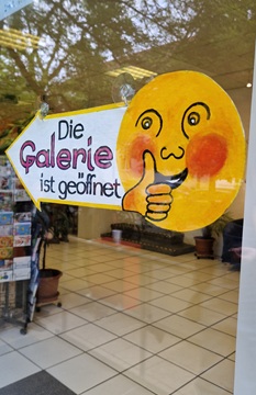 Hinweisschild am Fenster mit einem großen Smiley und der Aufschrift "Die Galerie ist geöffnet".