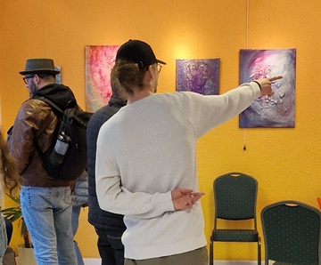 Ein Besucher der Ausstellung zeigt mit ausgestrecktem Arm auf ein abstraktes Gemälde.
