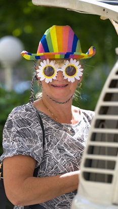 Eine Frau, verkleidet mit bunt gestreiftem Hut und Blumen-Sonnenbrille, lacht in die Kamera.