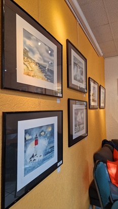 Seitliche Aufnahme einer der Ausstellungswände mit mehreren eingerahmten Aquarellen von Küstenlandschaften.