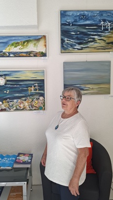 Ulrike Drobniewski steht vor vier ihrer Acrylgemälde, die alle Küstenlandschaften zeigen.