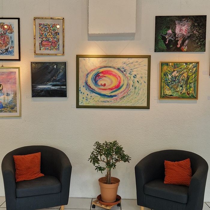 Bunte Kunstwerke hängen an einer Wand. Darunter stehen zwei gemütlich wirkende Sessel.