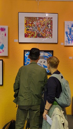 Zwei Personen stehen mit dem Rücken zum Betrachtenden vor zwei bunten Kunstwerken mit Fabelwesen.